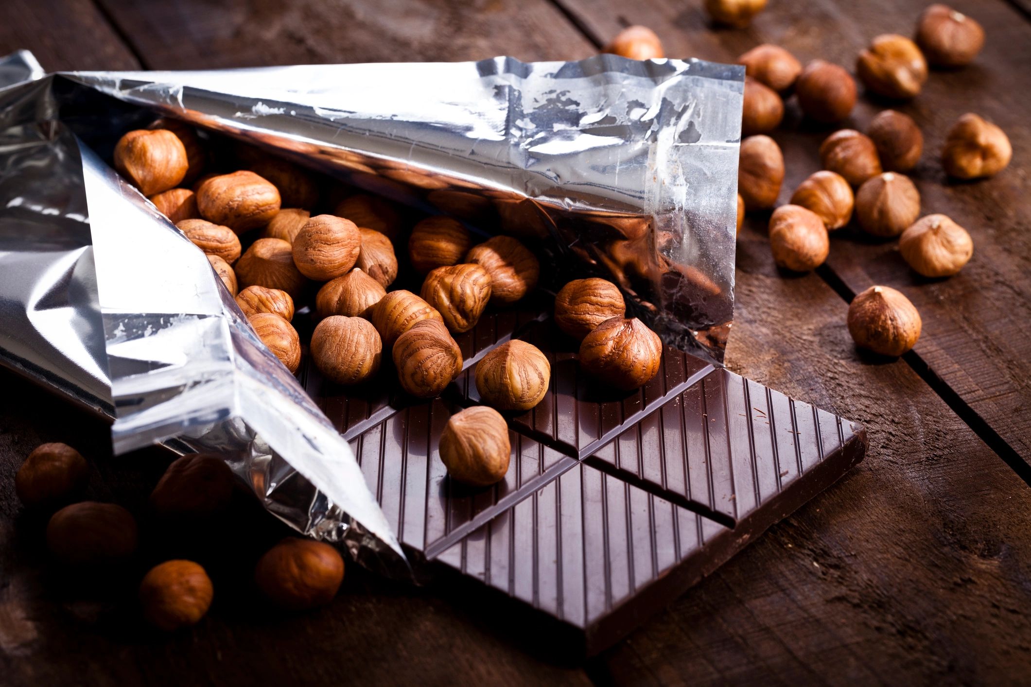 Chocolate bar partially unwrapped on a rustic table with hazelnuts